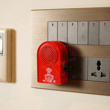 A red Gayatri Mantra Musical Chanting Speaker Box plugged into a wall socket, designed to play mantras for spiritual purposes.