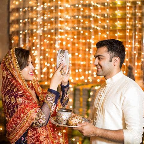 A couple performing karwa chauth rituals by seeing her husband through seive